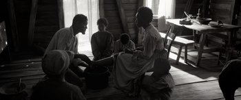 Movie still from “Emancipation” (2022), directed by Antoine Fuqua – A black and white photo of a group of people sitting around; Wide shot, High angle