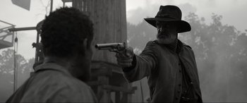 Movie still from “Emancipation” (2022), directed by Antoine Fuqua – An old man in a hat is holding a gun; Medium shot, Over the shoulder angle