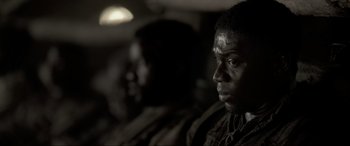 Movie still from “Emancipation” (2022), directed by Antoine Fuqua – A man sitting next to another man in a dark room; Close Up shot, Over the shoulder angle