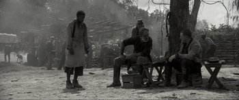 Movie still from “Emancipation” (2022), directed by Antoine Fuqua – A man sitting on top of a bench next to two other men; Wide shot, Over the shoulder angle
