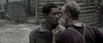 Movie still from “Emancipation” (2022), directed by Antoine Fuqua – Two men standing next to each other in front of a wooden fence; Close Up shot, Over the shoulder angle