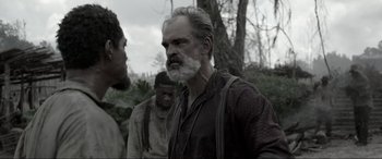 Movie still from “Emancipation” (2022), directed by Antoine Fuqua – A man with a gray beard is standing in front of two other men; Close Up shot, Over the shoulder angle