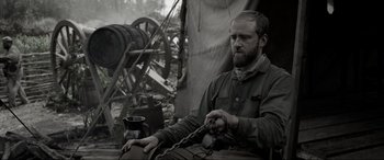 Movie still from “Emancipation” (2022), directed by Antoine Fuqua – A man chained to a chain sitting in front of an old steam engine; Medium shot, Over the shoulder angle