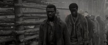 Movie still from “Emancipation” (2022), directed by Antoine Fuqua – Two black men standing next to each other in front of logs; Medium shot, High angle