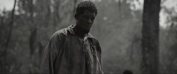 Movie still from “Emancipation” (2022), directed by Antoine Fuqua – A black and white photo of a man in a forest; Medium shot, Over the shoulder angle
