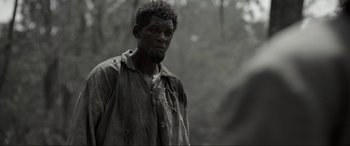 Movie still from “Emancipation” (2022), directed by Antoine Fuqua – A black and white photo of a man in the woods; Medium shot, Over the shoulder angle