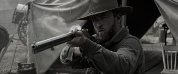 Movie still from “Emancipation” (2022), directed by Antoine Fuqua – A man with a beard and a hat is holding a gun; Close Up shot, Over the shoulder angle
