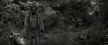 Movie still from “Emancipation” (2022), directed by Antoine Fuqua – A man standing next to some bushes and trees; Medium shot, Over the shoulder angle