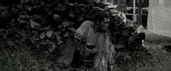 Movie still from “Emancipation” (2022), directed by Antoine Fuqua – A man sitting on the ground with a bowl in his hand; Medium shot, High angle