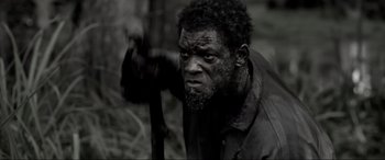 Movie still from “Emancipation” (2022), directed by Antoine Fuqua – A black and white photo of a man holding a stick; Close Up shot, High angle