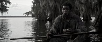 Movie still from “Emancipation” (2022), directed by Antoine Fuqua – A black and white photo of a man in a canoe; Medium shot, Low angle