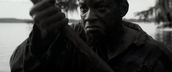 Movie still from “Emancipation” (2022), directed by Antoine Fuqua – A black and white photo of a man holding a wooden stick; Close Up shot, Low angle