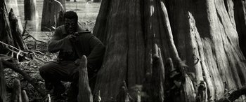 Movie still from “Emancipation” (2022), directed by Antoine Fuqua – A man sitting in front of a tree trunk; Wide shot, Low angle