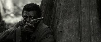 Movie still from “Emancipation” (2022), directed by Antoine Fuqua – A black and white photo of a man holding a gun; Close Up shot, Low angle
