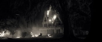 Movie still from “Emancipation” (2022), directed by Antoine Fuqua – A house on fire at night with a person riding a horse in front of it; Extreme Wide shot, Low angle