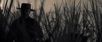 Movie still from “Emancipation” (2022), directed by Antoine Fuqua – A man with a hat and a gun standing in front of some bushes; Medium shot, Low angle