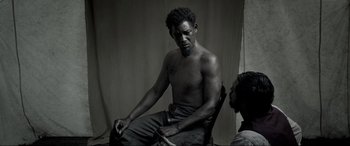 Movie still from “Emancipation” (2022), directed by Antoine Fuqua – A man sitting in a chair with a woman; Medium shot, High angle