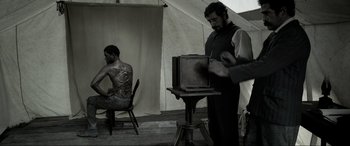 Movie still from “Emancipation” (2022), directed by Antoine Fuqua – A man standing next to a man sitting in front of a camera; Medium shot, Over the shoulder angle