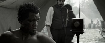 Movie still from “Emancipation” (2022), directed by Antoine Fuqua – A black and white photo of a man with a knife in his hand; Close Up shot, Over the shoulder angle