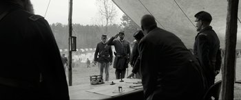 Movie still from “Emancipation” (2022), directed by Antoine Fuqua – A man saluting another man while another man looks on; Wide shot, Over the shoulder angle