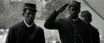 Movie still from “Emancipation” (2022), directed by Antoine Fuqua – A black and white photo of two men saluting; Close Up shot, Low angle