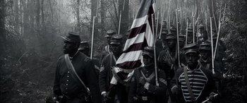 Movie still from “Emancipation” (2022), directed by Antoine Fuqua – A group of men in uniforms holding a flag; Medium shot, High angle