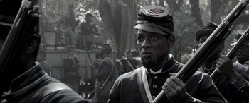 Movie still from “Emancipation” (2022), directed by Antoine Fuqua – A man in a civil war era uniform with other civil war reenactors in the background; Close Up shot, Over the shoulder angle