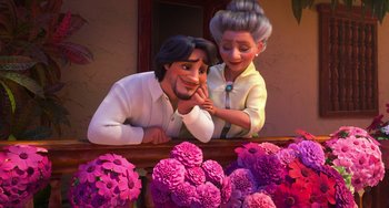 Movie still from “Encanto” (2021), directed by Charise Castro Smith – A man and a woman sitting next to each other in front of flowers; Medium shot, Low angle
