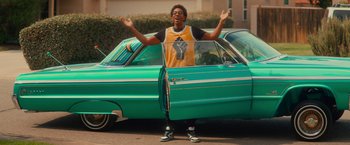 Movie still from “End of the Road” (2022), directed by Millicent Shelton – A man standing in front of a green car; Wide shot, Low angle