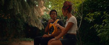 Movie still from “End of the Road” (2022), directed by Millicent Shelton – A man and a woman sitting on a bench smoking; Medium shot, Over the shoulder angle