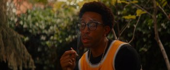 Movie still from “End of the Road” (2022), directed by Millicent Shelton – A man with glasses smoking a cigarette outside; Close Up shot, Low angle
