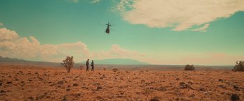 Movie still from “End of the Road” (2022), directed by Millicent Shelton – Two people standing in a field looking at a helicopter; Extreme Wide shot, Low angle