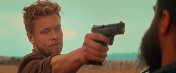 Movie still from “End of the Road” (2022), directed by Millicent Shelton – A person holding a gun; Close Up shot, Over the shoulder angle