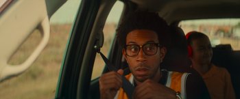 Movie still from “End of the Road” (2022), directed by Millicent Shelton – A man with glasses is holding a pair of scissors; Close Up shot, Over the shoulder angle