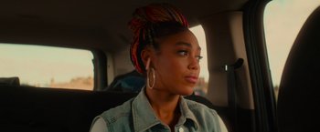 Movie still from “End of the Road” (2022), directed by Millicent Shelton – A woman sitting in the back of a car wearing ear buds; Close Up shot, Over the shoulder angle