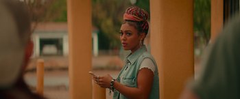 Movie still from “End of the Road” (2022), directed by Millicent Shelton – A young woman holding a cell phone while standing outside; Close Up shot, Over the shoulder angle