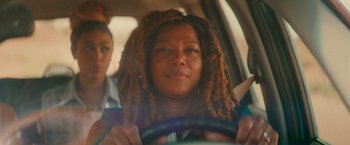 Movie still from “End of the Road” (2022), directed by Millicent Shelton – A woman with dreads sitting in the drivers seat of a car; Close Up shot, Over the shoulder angle