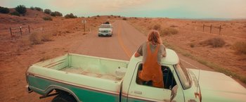 Movie still from “End of the Road” (2022), directed by Millicent Shelton – A truck driving down a road with a person in the back of the truck; Wide shot, High angle