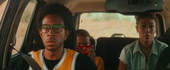 Movie still from “End of the Road” (2022), directed by Millicent Shelton – A man with glasses is sitting in the back of a car; Close Up shot, Over the shoulder angle