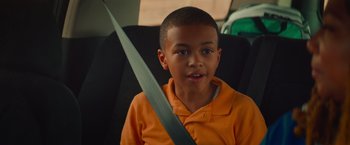 Movie still from “End of the Road” (2022), directed by Millicent Shelton – A boy sitting in the back of a car holding a seat belt; Close Up shot, High angle
