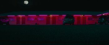 Movie still from “End of the Road” (2022), directed by Millicent Shelton – A car is parked in front of a building at night; Extreme Wide shot, Low angle