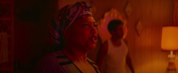 Movie still from “End of the Road” (2022), directed by Millicent Shelton – A woman with a headscarf in a dark room; Close Up shot, Over the shoulder angle