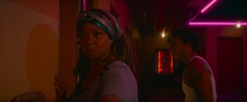 Movie still from “End of the Road” (2022), directed by Millicent Shelton – A woman with dreadlocks standing in a dark room; Medium shot, Over the shoulder angle