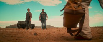 Movie still from “End of the Road” (2022), directed by Millicent Shelton – A man standing in the dirt with a gun in his hand; Wide shot, Low angle