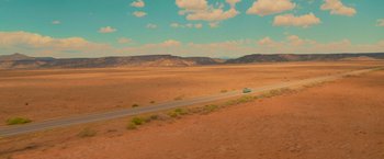 Movie still from “End of the Road” (2022), directed by Millicent Shelton – A car driving down a road in the middle of a desert; Extreme Wide shot, High angle