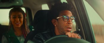 Movie still from “End of the Road” (2022), directed by Millicent Shelton – A person sitting in a car wearing glasses; Close Up shot, Over the shoulder angle