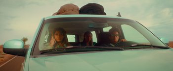 Movie still from “End of the Road” (2022), directed by Millicent Shelton – A group of people sitting in the back of a car; Medium shot, Low angle
