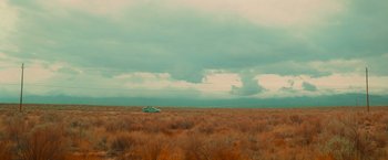 Movie still from “End of the Road” (2022), directed by Millicent Shelton – A car is parked in the middle of a grassy field; Extreme Wide shot, Low angle