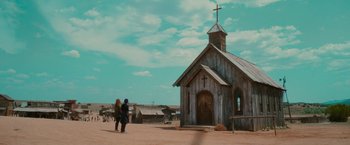 Movie still from “End of the Road” (2022), directed by Millicent Shelton – Two people standing in front of an old wooden church; Extreme Wide shot, Low angle