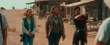 Movie still from “End of the Road” (2022), directed by Millicent Shelton – A group of people standing on top of a dirt field; Medium shot, Over the shoulder angle